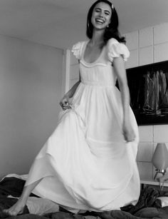 a woman in a white dress is standing on a bed and smiling at the camera