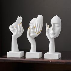 three white sculptures with gold rings on their hands and one holding the other's head