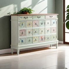 a white dresser with flowers painted on the drawers and plants in potted planter