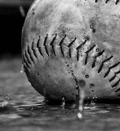 a black and white photo of a baseball in the water with drops of water on it