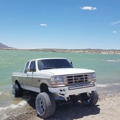 a white truck parked on top of a sandy beach next to the ocean with mountains in the background