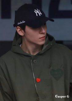 a young man wearing a black hat and green jacket with a red heart on it