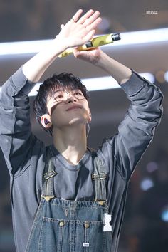 a young man holding his hands up to the sky while wearing overalls and an earbud