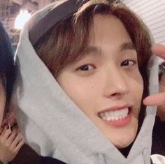 a young man is smiling and holding his hood up to his face while another person looks on