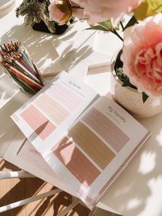 an open book sitting on top of a white table next to flowers and pencils