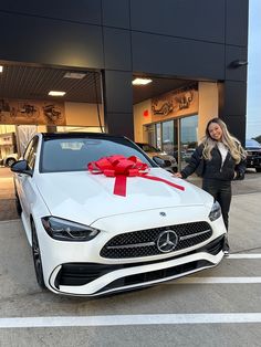 a woman standing next to a white car with a red bow on it