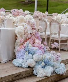 an arrangement of flowers and chairs on the steps at a wedding reception with white table cloths