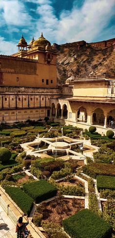 a person standing in front of a large building with many plants and bushes around it