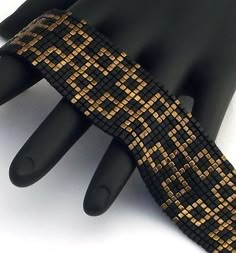 a close up of a hand wearing a black and gold bracelet