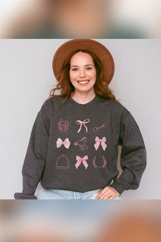 A smiling woman with long red hair wears a wide-brimmed brown hat and a dark gray sweatshirt. The sweatshirt features pink illu Coquette Sweater, Coquette Cowgirl, Pink Jumper, Pink Bows