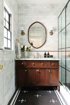 a bathroom with black and white tile flooring and a round mirror on the wall