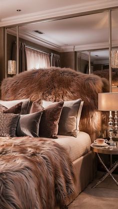 a bed with pillows and fur on top of it in a bedroom next to a mirror