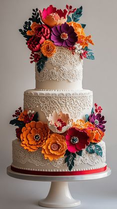 a three tiered wedding cake decorated with colorful flowers and lace, on a white pedestal