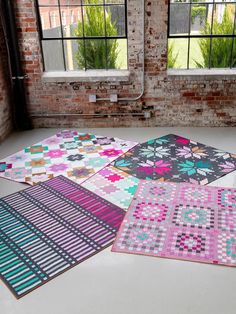 four different colored rugs are on the floor in front of a brick wall and windows