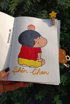 a hand holding an open book with a cartoon character on it