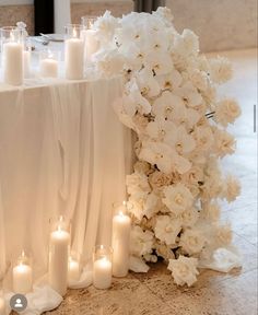 white flowers and candles are on the floor next to a table with a cloth draped over it