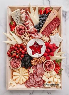 a wooden platter filled with cheese, meats, fruit and crackers on top of a marble counter