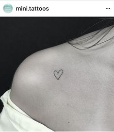 the back of a woman's shoulder with a small heart tattoo on it