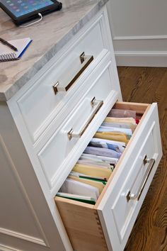 an open drawer in a kitchen next to a tablet and pen on a counter top