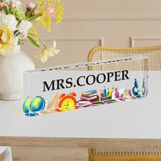 there is a sign that says mrs cooper next to a vase with flowers in it