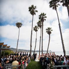 a wedding ceremony on the beach with palm trees and people sitting in chairs under them