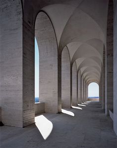 an empty walkway with arches and pillars leading to the ocean