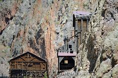 an old wooden structure on the side of a mountain next to a building in front of a cliff