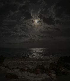 the moon is shining over the ocean on a cloudy night