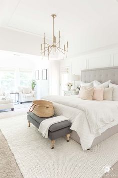 a large white bed sitting in a bedroom next to a chandelier and chair