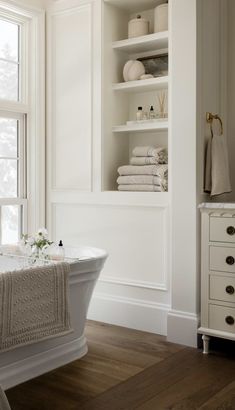 a white bath tub sitting under a window next to a shelf filled with towels and other items