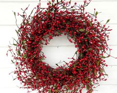 a red berry wreath hanging on the side of a white wall with green leaves and berries