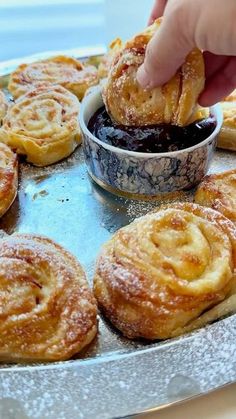 a person dipping some food into a bowl on top of a pan filled with pastries