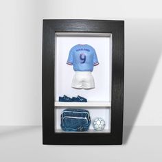 a black framed display case with a soccer jersey and other items in it on a white surface