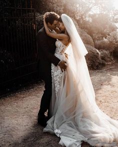 a bride and groom embracing each other in front of a fence with the sun shining on them