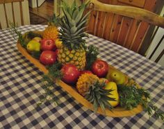 a wooden boat filled with lots of fruit on top of a checkered table cloth