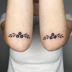 two women with matching tattoos on their arms, both have small flowers and leaves tattooed on them