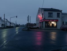 an empty street at night with cars parked in front of the building and lights on