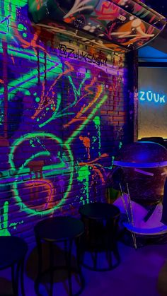 a room with neon lights and graffiti on the walls, along with tables and stools