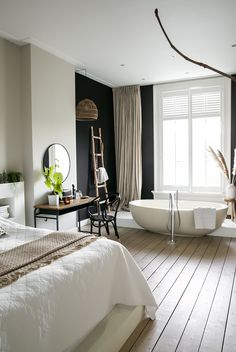 a large white bath tub sitting next to a bed in a room with wooden floors