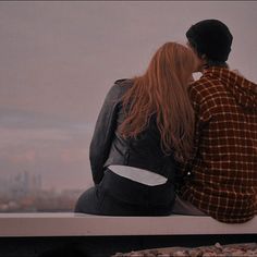 two people sitting on a ledge looking at the city