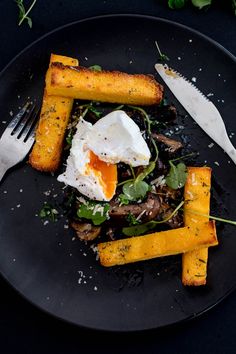 a black plate topped with vegetables and an egg on top of it next to a knife