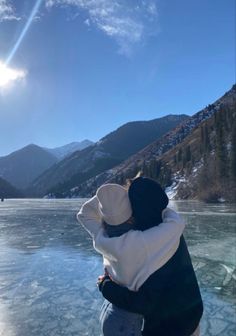 a person hugging another persons back on the frozen water in front of mountains and trees