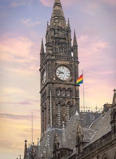 a large building with a clock on it's face and a rainbow flag flying in the background