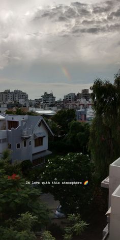 a rainbow is seen in the sky over some buildings and trees on a cloudy day