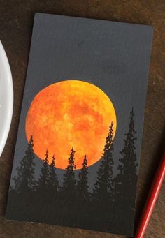 a painting of a full moon with trees in the foreground and a red pencil next to it