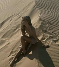 a woman sitting on top of a sandy beach next to a wave covered sand dune