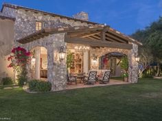 an outdoor patio with chairs and tables next to a stone building at night in the evening