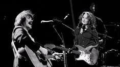 two people singing and playing guitars on stage