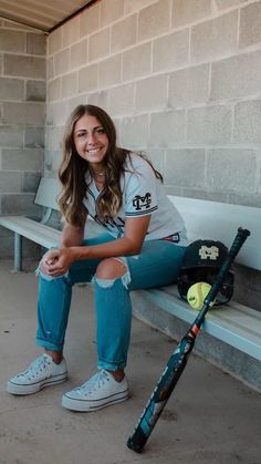 a woman sitting on a bench with a baseball bat and ball in her hand,