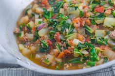 a white bowl filled with soup and vegetables on top of a tablecloth next to a spoon